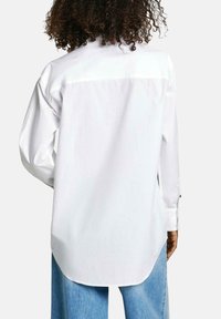 Camicia bianca a maniche lunghe con orlo curvo, dotata di polsini con bottone e un dettaglio a yoke sul retro. Realizzata in morbido cotone.