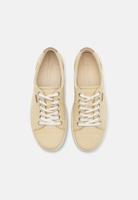 Beige läder sneakers med vita snörningar, rund tå och minimalistisk design. Har metalöglor och en tanfärgad accent vid hälen.
