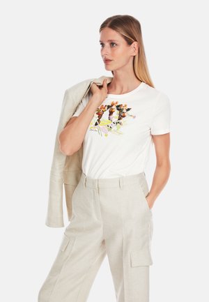 Weißes Baumwoll-T-Shirt mit einem bunten Druckdesign, das Blumen und Tiere zeigt, kombiniert mit hellbeigen Leinenhosen und einem passenden Blazer.