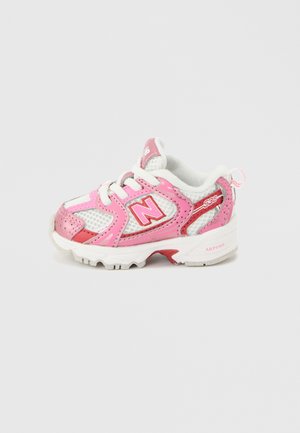 Hvid og lyserød toddler-sneaker med New Balance "N"-logo, mesh-stof og polstret sål, set fra ydersiden på en lys baggrund.