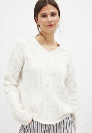 Weißer, gestrickter Pullover mit V-Ausschnitt, der über Kabelstrickdetails und gerippte Bündchen verfügt. Das Material wirkt weich und strukturiert.