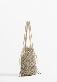 Beige neuleverkko laukku, jossa on punotut kahvat, nyöri suljenta ja mustat helmi korostukset. Pehmeä rakenne ja avoin muotoilu ilmanvaihtoa varten.
