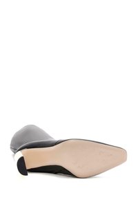 Stivale alto in pelle nera con tacco a spillo, punta affusolata e tomaia liscia, e suola beige. Presenta un'accente in argento sul tallone.