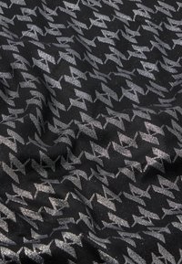 Sort stof med et sølvfarvet hundetænder-mønster, der har en glat tekstur og en subtil glans. Designet gentages ensartet over hele materialet.