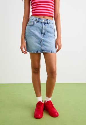 Denim mini skirt in light blue with a fitted design, five-pocket styling, and a raw hem. Paired with bright red sneakers and white socks.