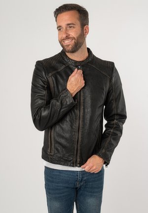 Schwarze Lederjacke mit gerippten Schulterakzenten, Stehkragen und Reißverschlüssen, kombiniert mit blauen Jeans.