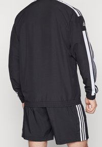 Black athletic tracksuit with white side stripes, made of smooth fabric; features elastic waistband and cuffs, designed for comfort and mobility.