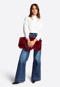 Weiße Bluse mit Spitzenkragen, burgunderfarbener Kunstfell-Clutch, hoch taillierte blaue Jeans mit weitem Bein und schwarze spitz zulaufende High Heels.