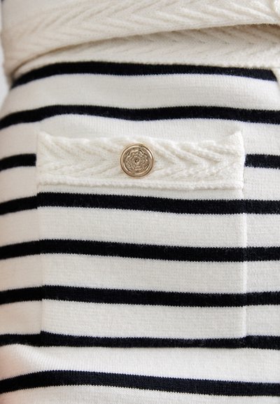 Stribet sweater i hvid og marineblå farve med en lomme, der er pyntet med en rund, dekorativ gylden knap. Blødt strikstof.