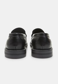Zapatos de cuero negro con un acabado suave, tacones redondeados y suelas de goma bajas, que presentan costuras decorativas a lo largo de las costuras.