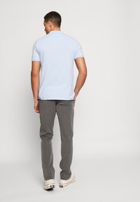 Sky blue polo shirt with short sleeves, paired with gray trousers and beige sneakers. Simple design with a straight silhouette.