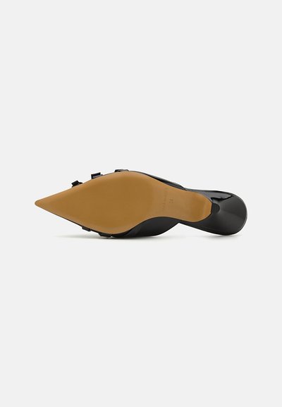 Zapato de charol negro de tacón alto con punta afilada y suela de goma beige claro que presenta sutiles detalles de marca.