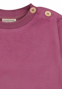Maglietta a maniche lunghe di colore viola con una texture morbida; scollatura rotonda con due bottoni di legno sulla spalla. Etichetta con la scritta "loud + proud."