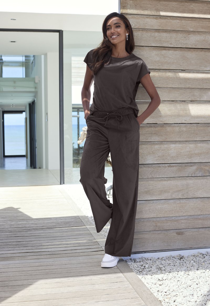 Dark brown, short-sleeve top paired with matching drawstring pants, designed for comfort. Plain texture with a relaxed fit; styled with white sneakers.