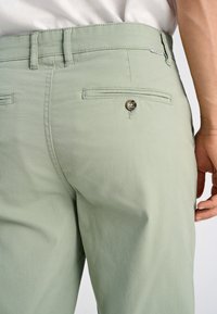 Jasnozielone spodnie wykonane z miękkiej bawełny, z tylną kieszenią zapinaną na guzik i dopasowanym krojem.