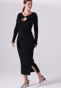 Čierne rebrované pletené šaty s dlhými rukávmi, s výstrihom na kľúč a bočnými rozparkami. Kombinované s lesklými striebornými topánkami na podpätku.
