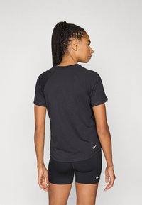 Μαύρο αθλητικό μπλουζάκι με κοντά μανίκια raglan, κατασκευασμένο από απαλό ύφασμα· διαθέτει μικρό λευκό λογότυπο στο πίσω μέρος στο τελείωμα.