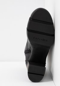 Semelle d'une botte en cuir noir montrant des rainures profondes, un talon bloc, une fermeture éclair latérale et le logo "CAFéNOIR" avec la taille 37 embossée.