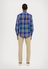 Långärmad rutig skjorta i blå, grön, gul och röd randning; matchad med beige byxor och svartvita sneakers.