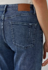 Donkerblauwe denim jeans met een leren label "s.Oliver" op de achterband, voorzien van een enkele achterzak met stikdetails.