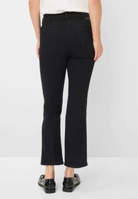 Zwarte flared jeans met een gemiddelde taillehoogte, voorzien van twee achterzakken en een gladde textuur. De zoom eindigt net boven de enkel.