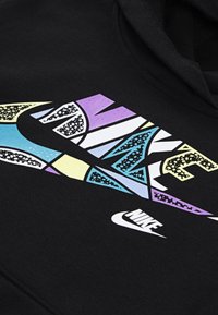 Črna kapuca z večbarvno grafiko, ki vsebuje Nike logotip in stilizirane črke v vijolični, modri in rumeni barvi z teksturiranimi vzorci.