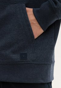 Felpa blu navy con tasca a marsupio, polsini a costine e un'etichetta del marchio sull'orlo con una finitura testurizzata.