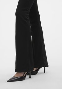Black flared pants paired with pointed-toe black heels. Pants feature a smooth texture, while heels have a sleek design and slender stiletto.