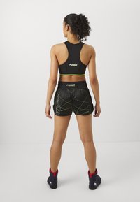 Black sports bra with green accents, paired with shiny black shorts featuring green line patterns. Worn with black boots highlighted in red.