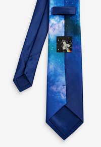 Silk tie featuring a gradient of blue and purple galaxy print, with a black patch depicting a rocket on a starry background.