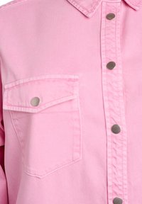 Rozā džinsa krekls ar klasisku apkakli, krūšu kabatu un sudrabotiem pogām priekšpusē. Gluda tekstūra, ikdienišķs dizains.