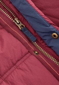 Burgundi és tengerészkék cipzáros felsőruha, fényes arany cipzárral, kontrasztos varrással és kék textil húzózsinórral. Sárgarézből készült patentgomb részlet.