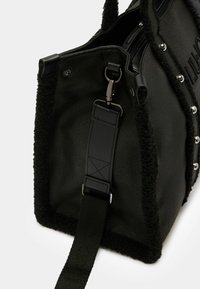 Sac à main en cuir noir avec des accents en peluche, des clous en argent et une bandoulière réglable. Comprend un dessus zippé et une surface texturée.