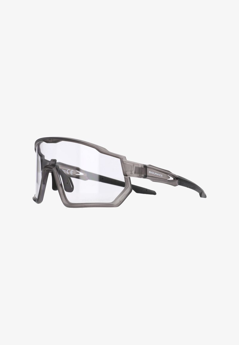 Harmaat urheilulliset aurinkolasit, joissa on puolirajaton muotoilu, kirkkaat linssit ja teksturoidut, kumiset tempaukset. Sivussa logo.