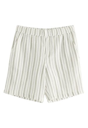 Dreng står iført lysefarvet, lodret striped kortærmet skjorte og matchende shorts med sorte sandaler, hænderne i lommerne.