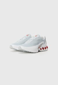 Light gray mesh athletic shoes with red accents, featuring a padded collar, white sole, and distinctive bubble-like cushioning on the heel.