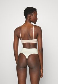Beige ribbattu lanti, jossa on ohuet hihnat, ja vaaleat korkeavyötäröiset alushousut, joissa on pehmeä tuntuma ja saumaton muotoilu.