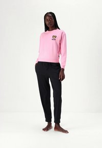 Pink sweatshirt with bear logo on chest, paired with black tapered pants. Soft fabric, ribbed cuffs, and waistband detail.