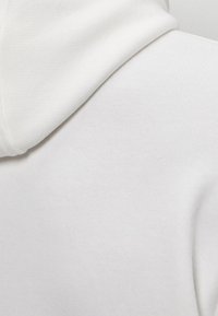 Felpa bianca in cotone con una texture liscia, tessuto morbido e un cordoncino al collo, con una forma aderente sulle spalle.