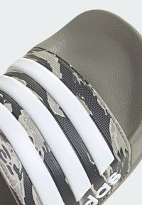 Sandal slide in bianco e nero con tre strisce bianche, una parte superiore texturizzata e una suola in gomma grigia con un motivo mimetico.