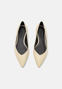 Bezešvé kožené boty v béžové barvě s špičatou špičkou, otevřenými bočními stranami a černým interiérem. Logo značky "HUGO" je vyraženo uvnitř.