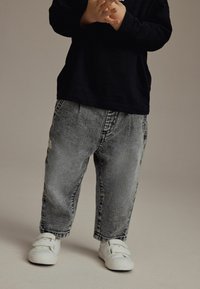 Jean baggy taille enfant en denim noir délavé, avec une texture douce, présentant une coupe droite, des poches latérales et une petite étiquette sur la taille.