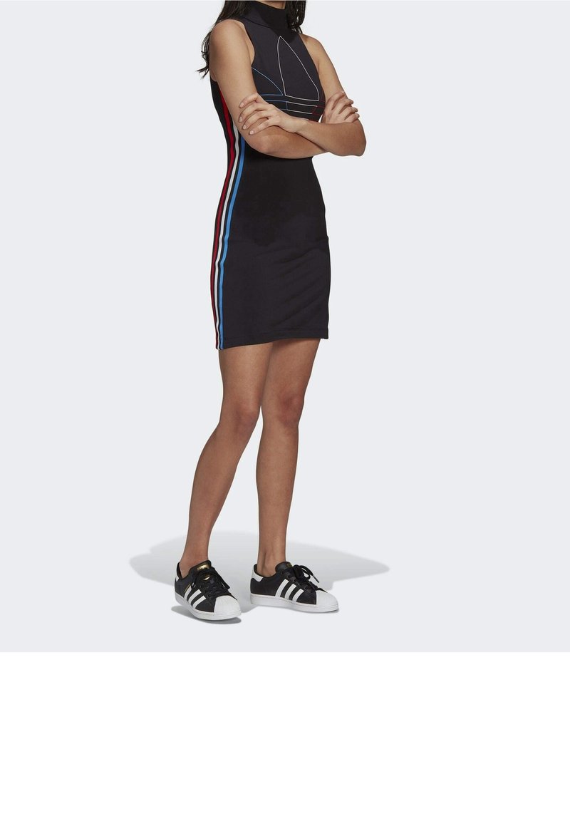 Černé bezrukávové šaty s vysokým límcem, s červenými a modrými postranními pruhy. Spárováno s černobílými teniskami. Hladká textura.