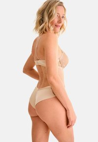 Set di lingerie beige con corpetto trasparente ricamato, spalline regolabili e slip a vita alta, che mette in risalto una texture liscia.