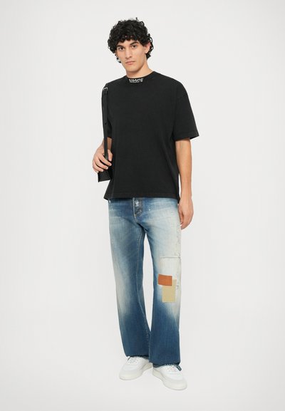 T-shirt di cotone nera con logo sul colletto, abbinata a jeans chiari strappati con dettagli in patch. Sneakers bianche completano il look.