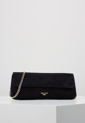 Zwarte suèdé clutch met gouden kettingriem en goudkleurig "Dune"-logo aan de voorkant, tentoongesteld op een witte sokkel tegen een effen achtergrond.