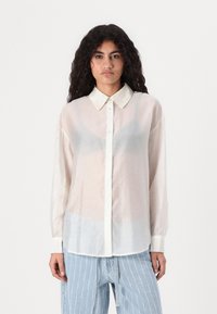 Gjennomsiktig hvit skjorte med krage, pyntet med små prikker, stappet ned i lyseblå stripete jeans. Lange ermer, myk tekstur.