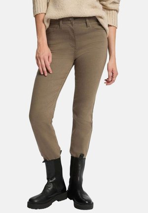 Pull en maille beige associé à un pantalon olive moulant et des bottes en cuir noires mi-mollet avec des semelles épaisses.