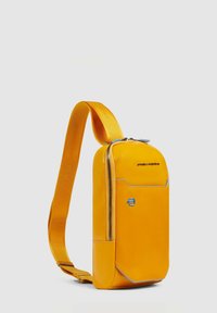 Gele synthetische schoudertas met een gladde textuur, ritssluiting en blauwe accenten. Voorzien van een schouderriem om te dragen.