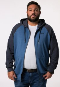 Blauwe en marinekleurige ritssluiting hoodie met een buidelzak, trekkoordcapuchon en contrasterende raglanmouwen. De stof lijkt zacht en textuur te hebben.